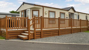 A single-story mobile home with a wooden deck, a front door, and a small porch. - 2 bedroom accommodation in Carnaby, near Bridlington (Carnaby, near Bridlington)