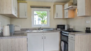 A compact kitchen with white cabinets, a microwave, a stove, and a sink. - 2 bedroom accommodation in Carnaby, near Bridlington (Carnaby, near Bridlington)