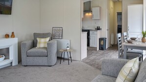 A modern living room with a grey sofa, a small round table, and a kitchen in the background. - 2 bedroom accommodation in Carnaby, near Bridlington (Carnaby, near Bridlington)