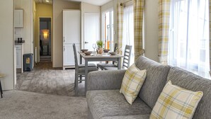 A living room with a grey sofa, a dining table with chairs, and a kitchen area in the background. - 2 bedroom accommodation in Carnaby, near Bridlington (Carnaby, near Bridlington)