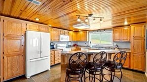 Una cocina con armarios de madera, un refrigerador blanco, un microondas y una isla grande con cuatro sillas.