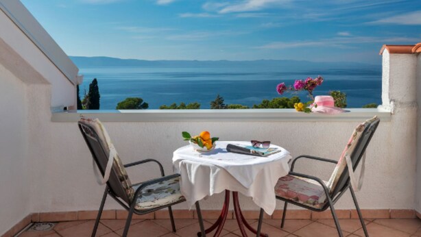A balcony with a table and chairs, overlooking a scenic view of the sea and distant mountains. - Apartments Lili Two Bedroom Apartment Sea View (Podgora)