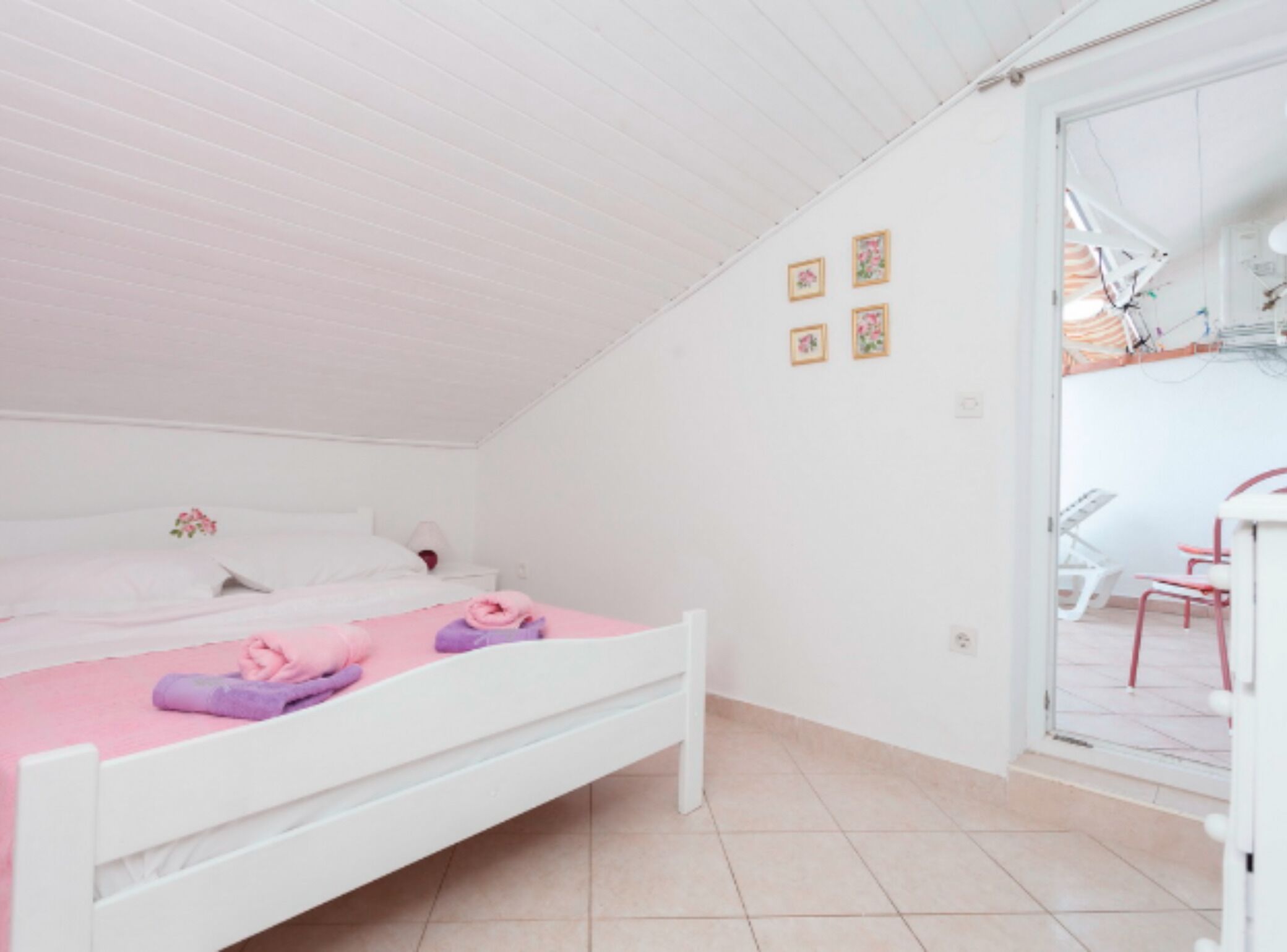 Un dormitorio con cama blanca, ropa de cama rosa y un escritorio pequeño con una silla.