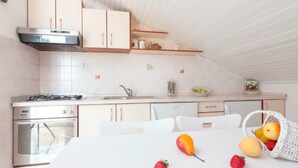 A kitchen with white cabinets, a stove, and a sink. There are fruits on the table and a basket with more fruits. - Apartments Lili Two Bedroom Apartment Sea View 3 (Podgora)