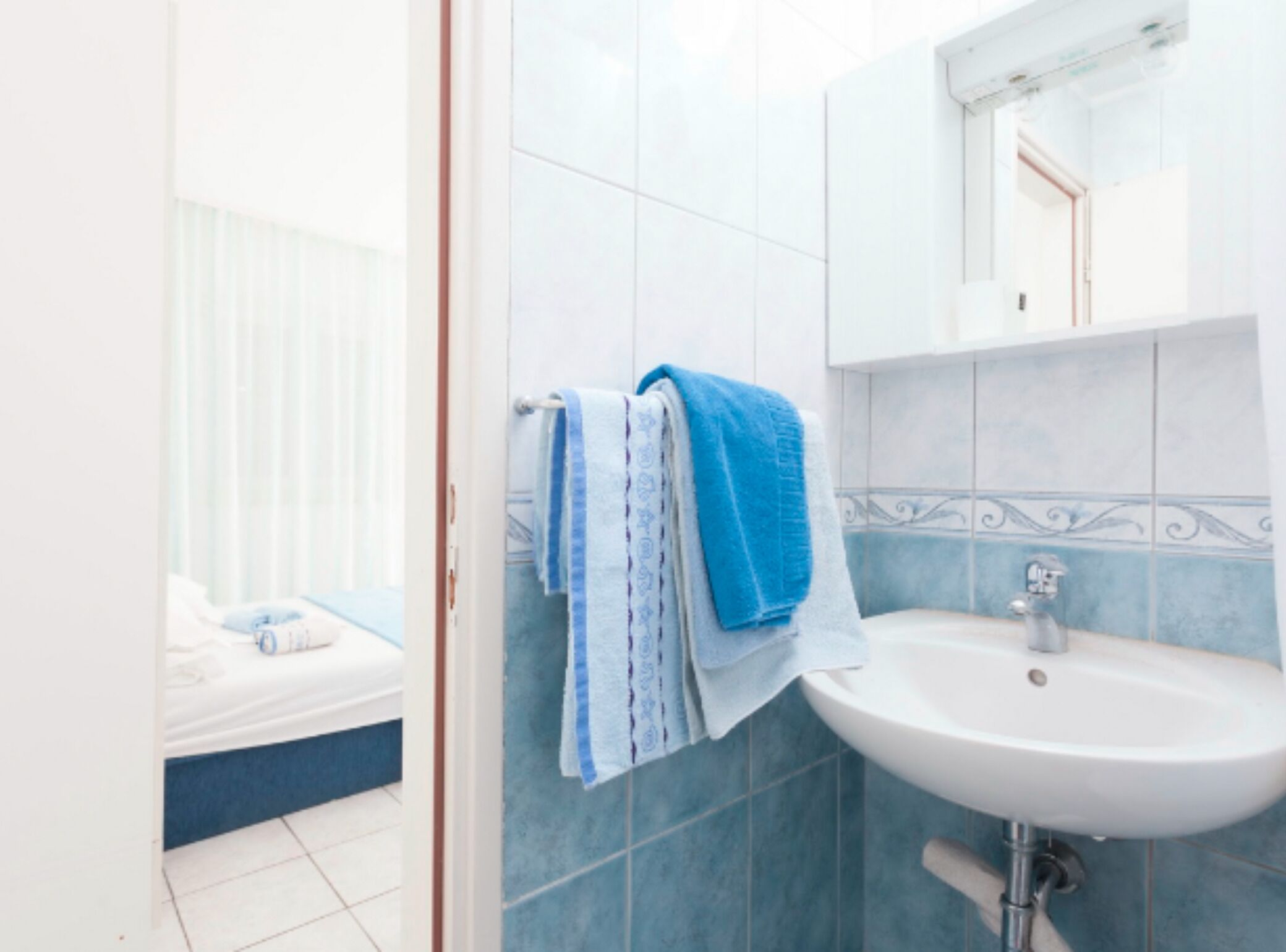A bathroom with a white sink, blue tiles, and a mirror above it.