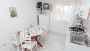 Una cuina petita i neta, amb armaris blancs, una cuina de gas i un rentatàs. Hi ha una taula de dinar amb cadires i una televisió petita sobre una estantàlia.