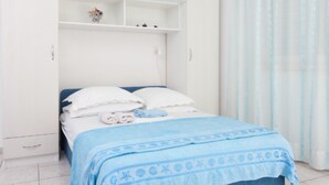 Un dormitori amb un llit, un armari blanc i una petita estant amb objectes decoratius.
