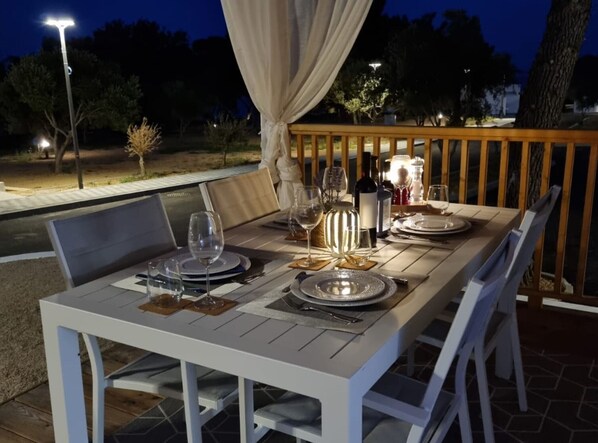 An outdoor dining area with a table set for four, surrounded by white chairs, under a canopy.