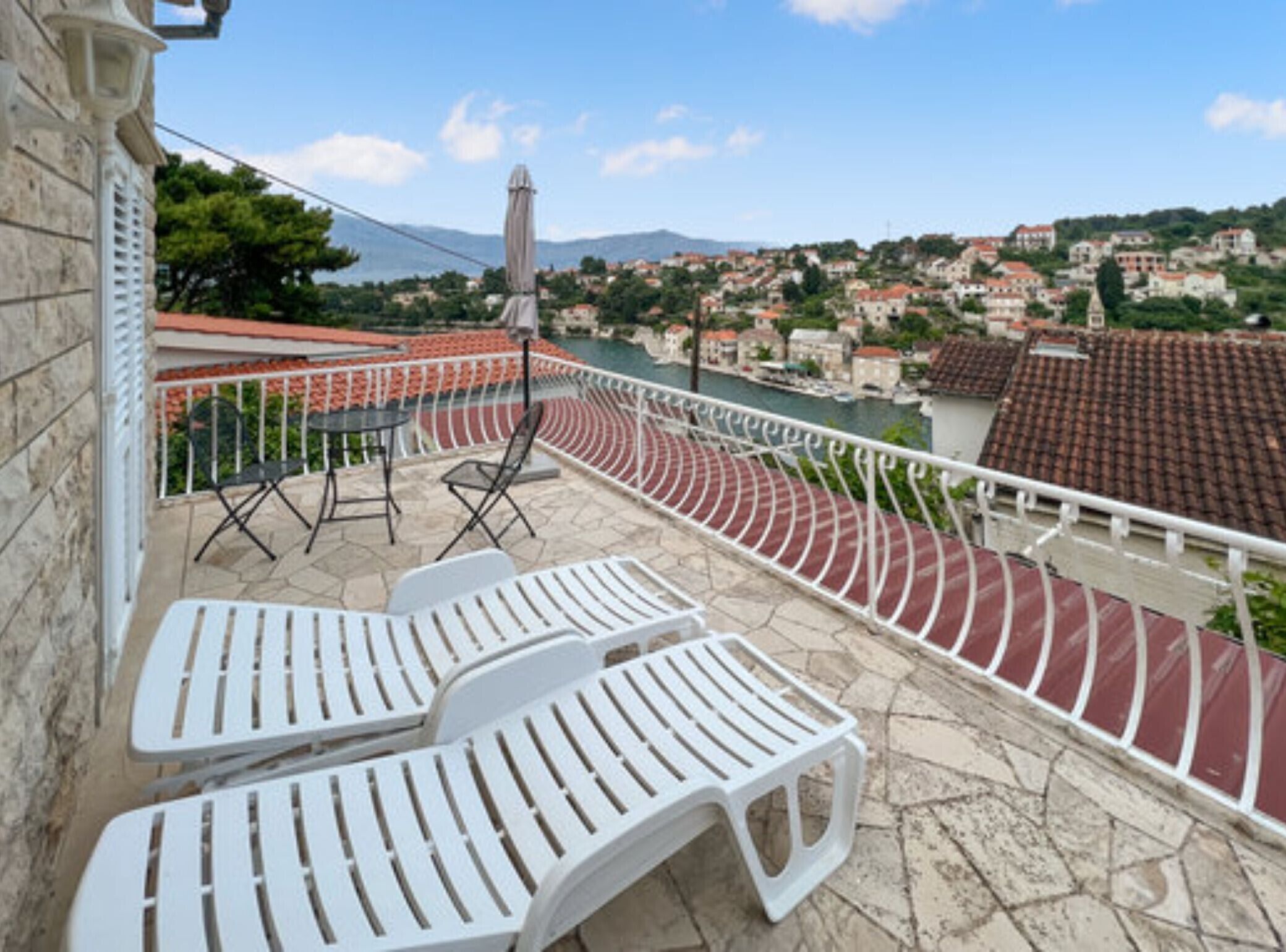 A terrace with white lounge chairs and a view of a coastal town.