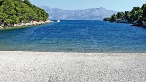A pebble beach with clear blue water, surrounded by green hills and mountains in the background. - Holiday Home Aurora - Three bedroom Holiday Home (Postira)