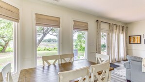 A dining area with a wooden table and white chairs, large windows with beige blinds, and a grey sofa in the background. - Walk to Marina: Pet-Friendly Little River Home! (Little River)