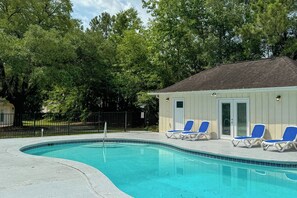 Ein Schwimmbad mit blauen Liegestühlen, ein kleines Gebäude mit einer Tür und Bäume im Hintergrund.