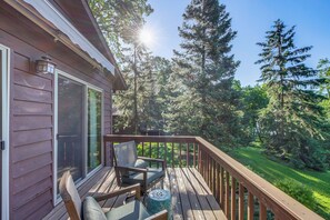 A wooden deck with a chair and a small table, overlooking a lush green landscape and tall trees. - Beach & Lake Access: Brainerd Townhome (Brainerd)