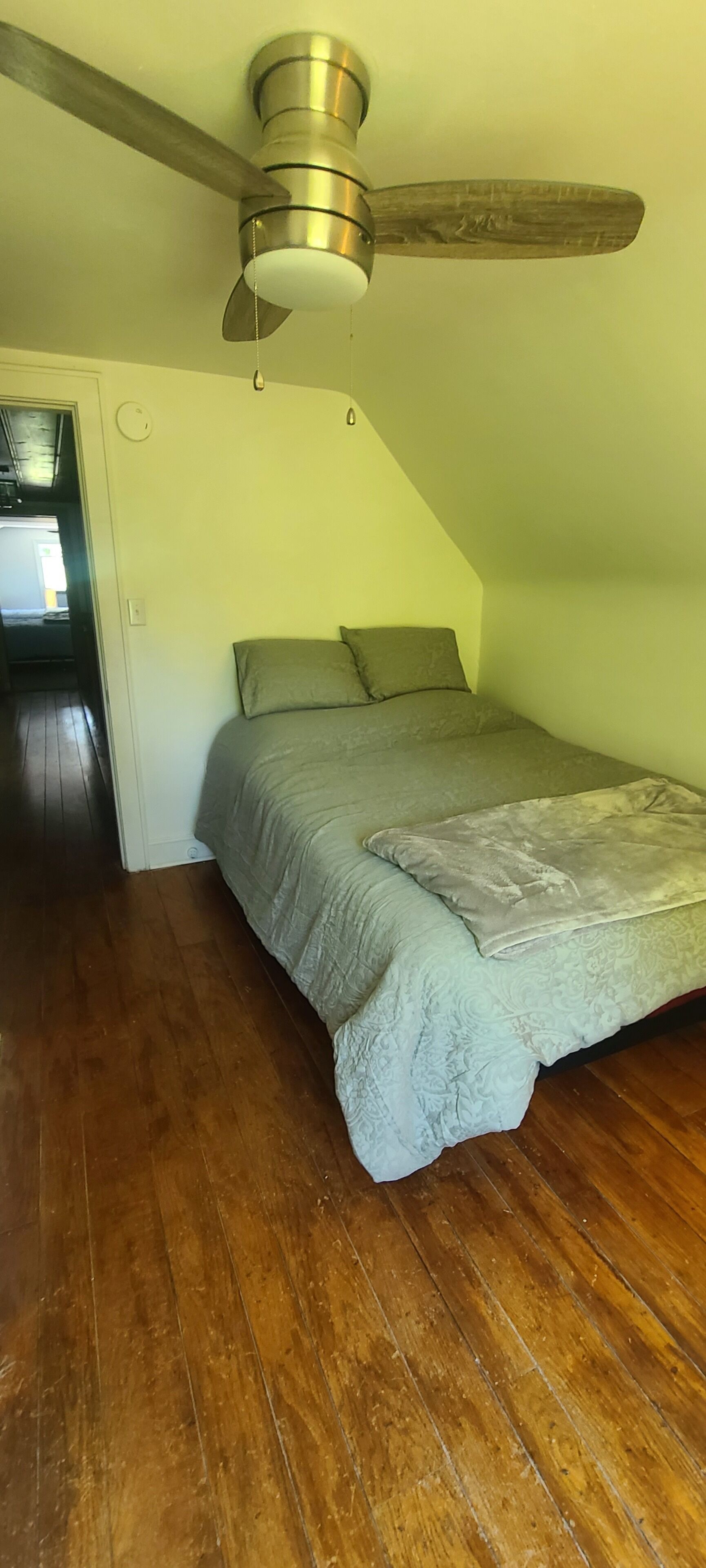 A bedroom with a wooden ceiling fan, a bed with a patterned bedspread, and a wooden floor.