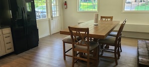 Een eetruimte met een houten tafel en stoelen, een zwarte koelkast en een brandblusser aan de muur.