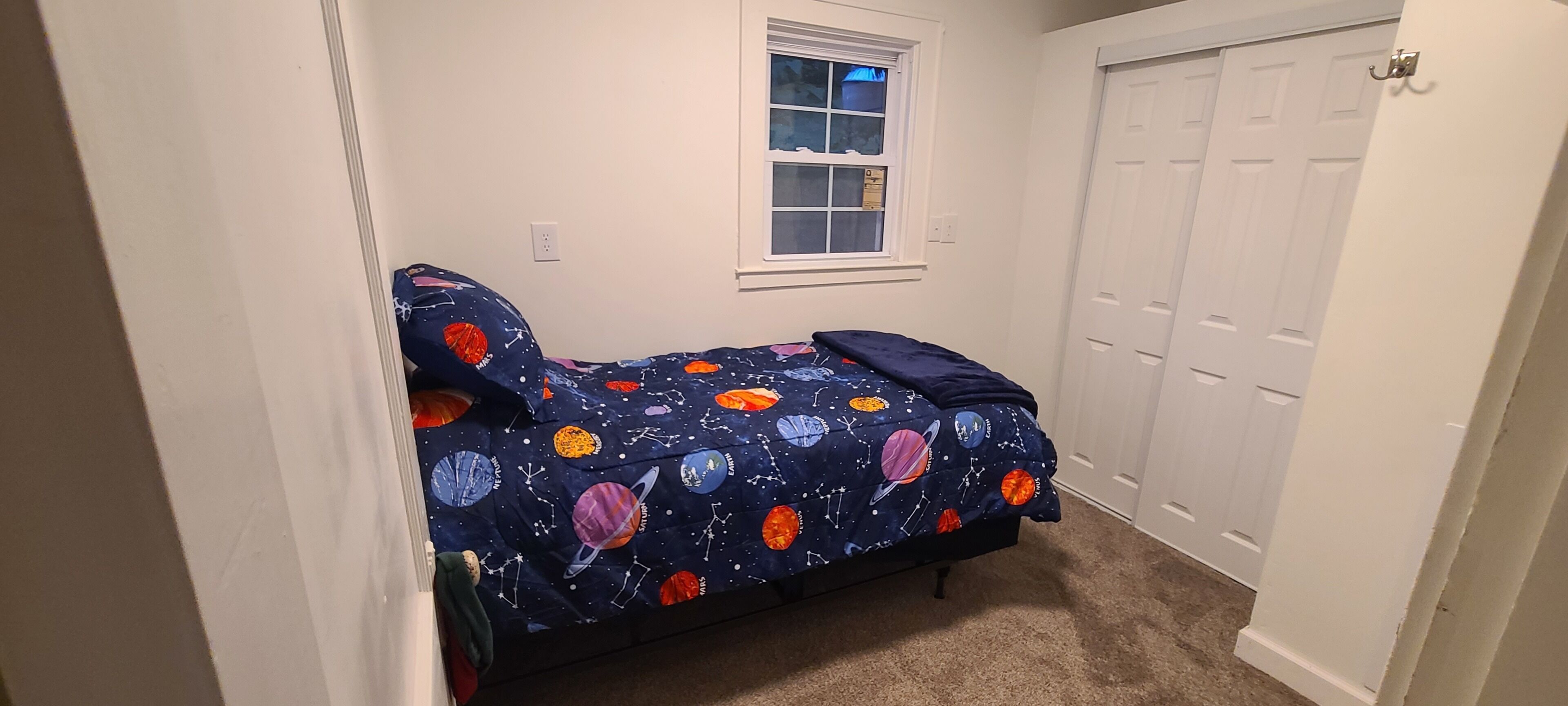 A small bedroom with a bed, a window, and a closet.