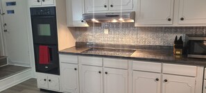Een keuken met witte kasten, een zwarte oven, een roestvrijstalen magnetron en een betegelde achterwand.
