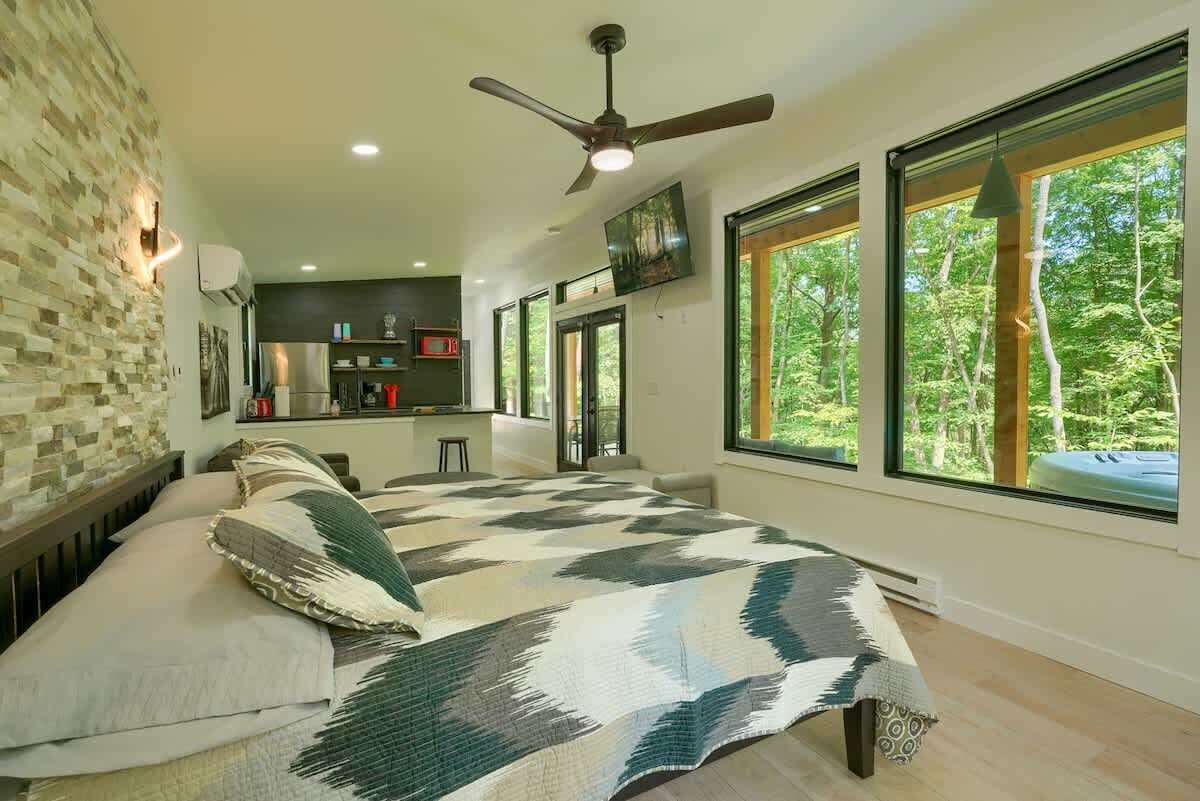 A bedroom with a large bed, a ceiling fan, and a view of the outdoors through large windows.