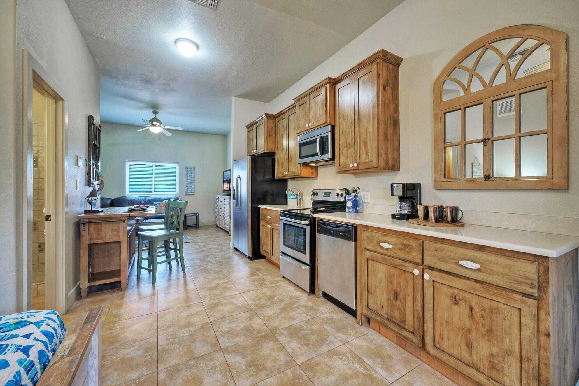 A kitchen with wooden cabinets, a microwave, a refrigerator, a stove, and a dishwasher. There is a window with blinds and a ceiling fan.