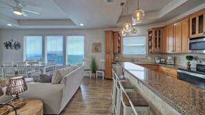 A modern kitchen with wooden cabinets, a granite countertop, and a built-in microwave. - Beach Boardwalk, Pool Access & Ocean Views Coral Reef by Avantstay (Port Aransas)