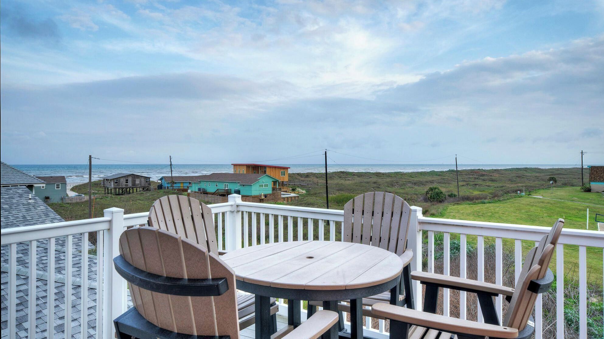 A deck with a table and chairs overlooking a beach and houses.
