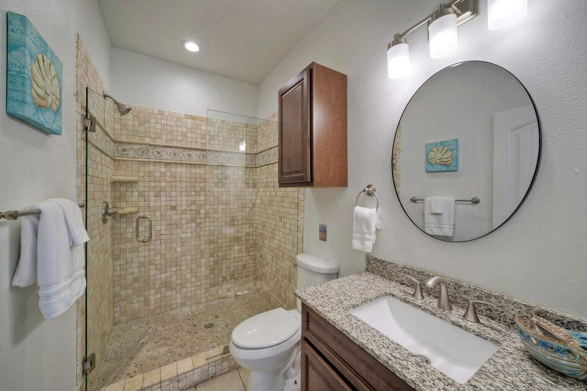 A bathroom with a glass shower enclosure, a toilet, a sink with a granite countertop, and a large mirror.