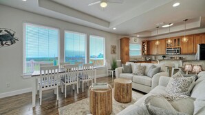 A spacious living room with a dining area, kitchen, and large windows with blinds.
