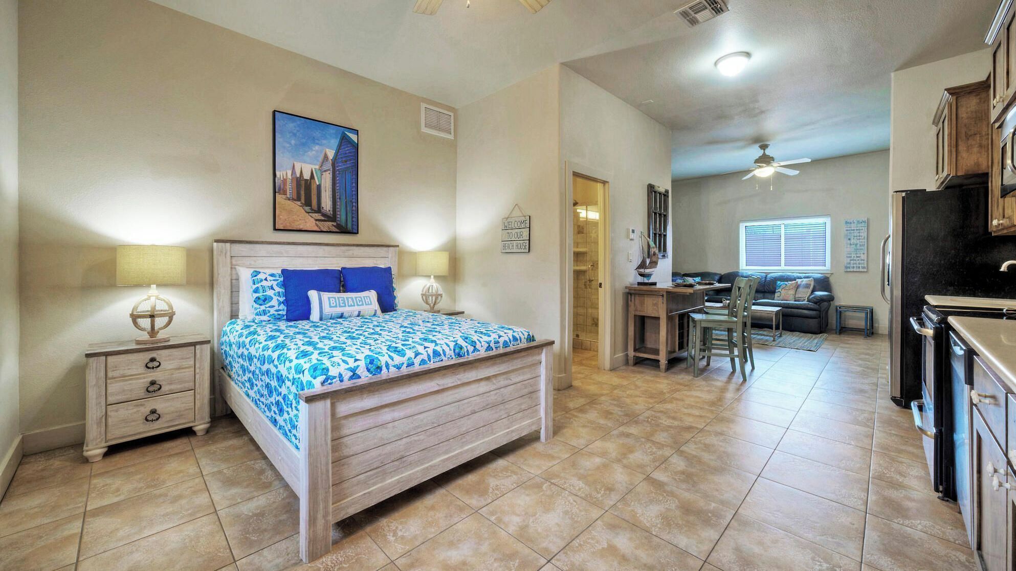 A bedroom with a bed, bedside tables, a desk, and a kitchenette.