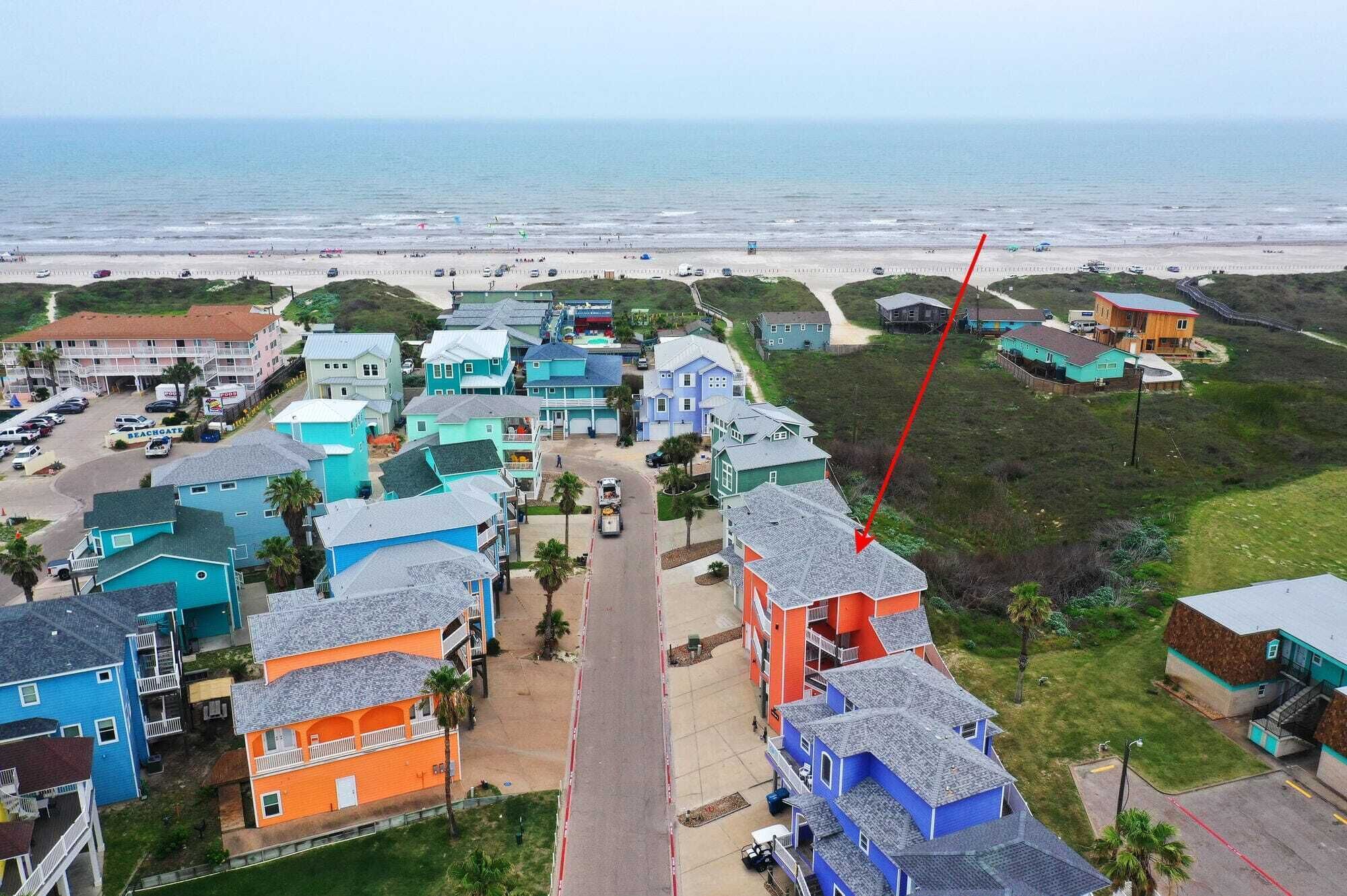 A coastal residential area with colorful houses, a beach in the background, and a red arrow pointing to a specific location.