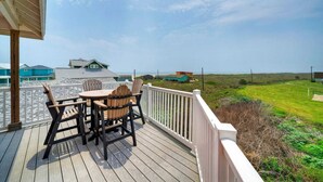 A wooden deck with a table and chairs, overlooking a grassy landscape and buildings.