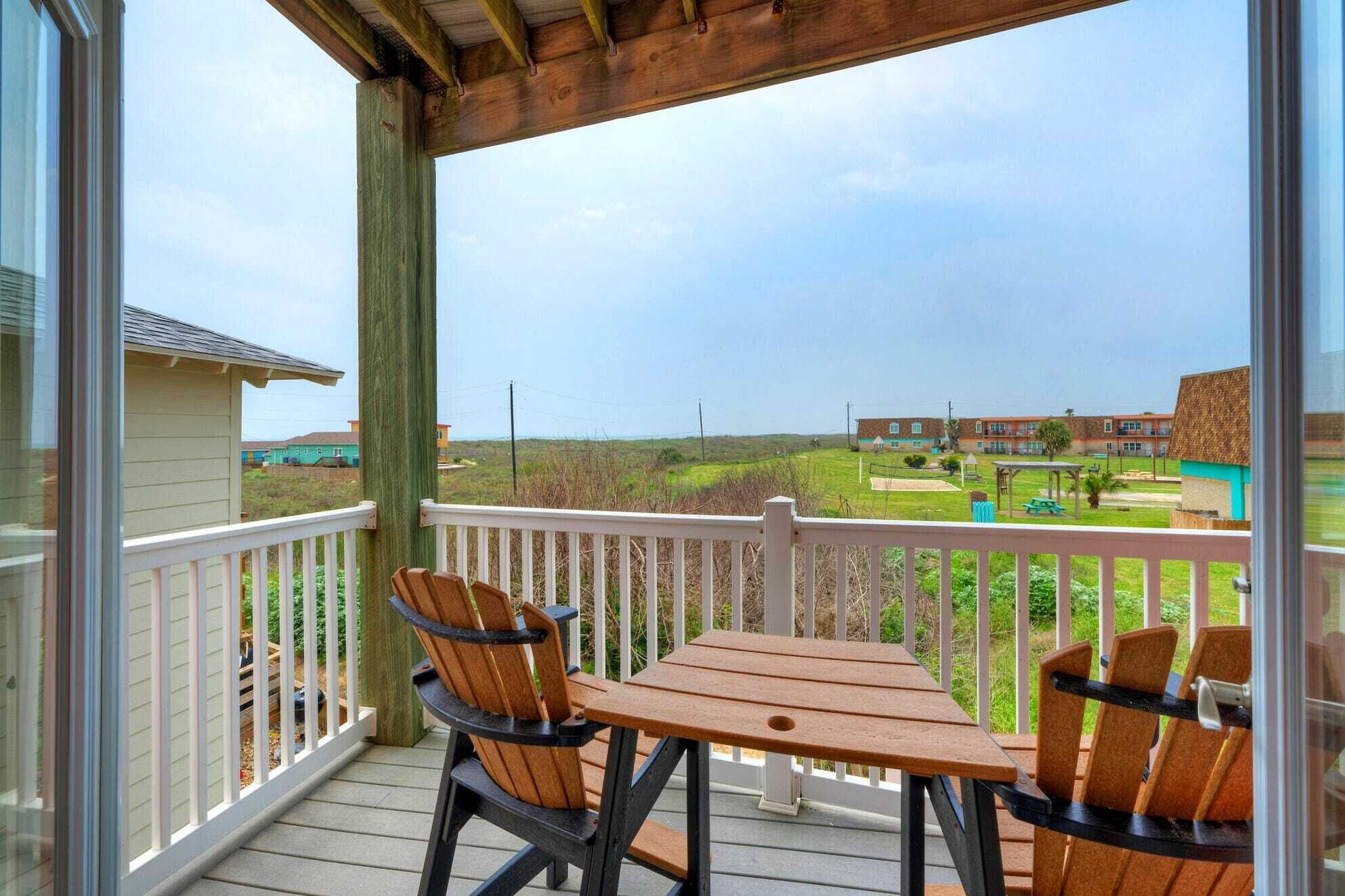 Une terrasse en bois avec une table et des chaises, d’où l’on a vue sur un terrain de golf et des bâtiments.