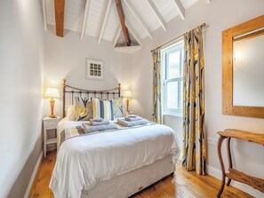 Un dormitorio con cama, mesitas de noche, lámparas, una ventana con cortinas y techo de madera.