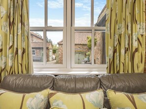 A room with a leather sofa, floral curtains, and a view of a brick building through large windows.