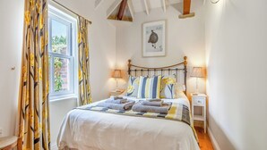 Une chambre à coucher comprenant un lit, deux tables de chevet, une fenêtre avec des rideaux, un tableau accroché au mur et un plafond avec des poutres apparentes.