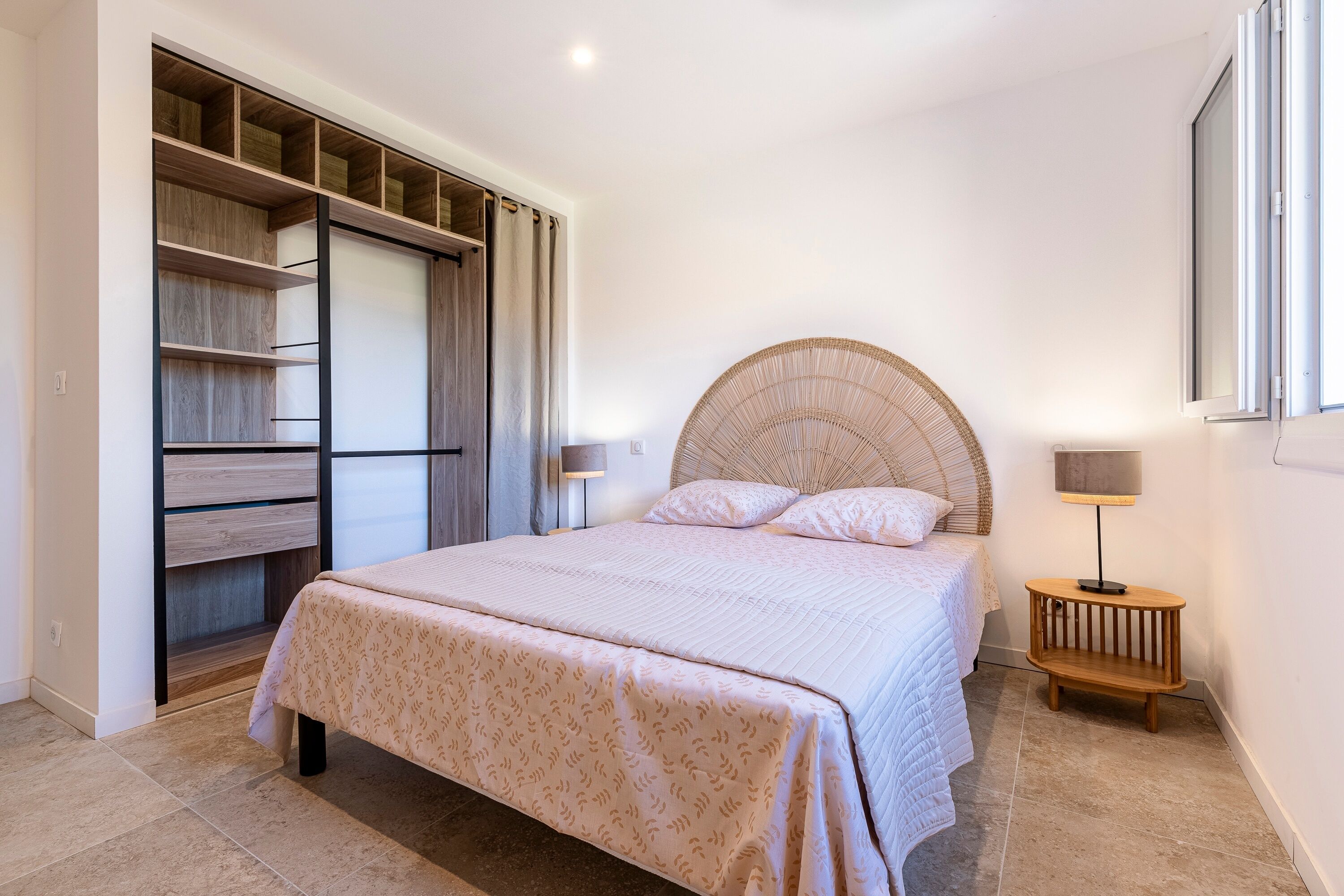 A bedroom with a bed, a bedside table, a lamp, a wardrobe, and a window.