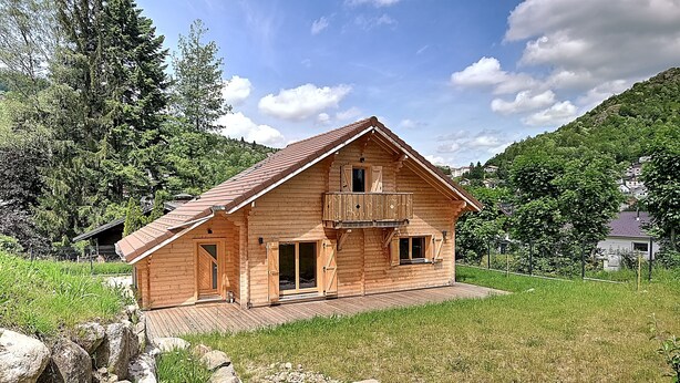 A wooden cabin with a balcony, surrounded by a grassy area and mountains.