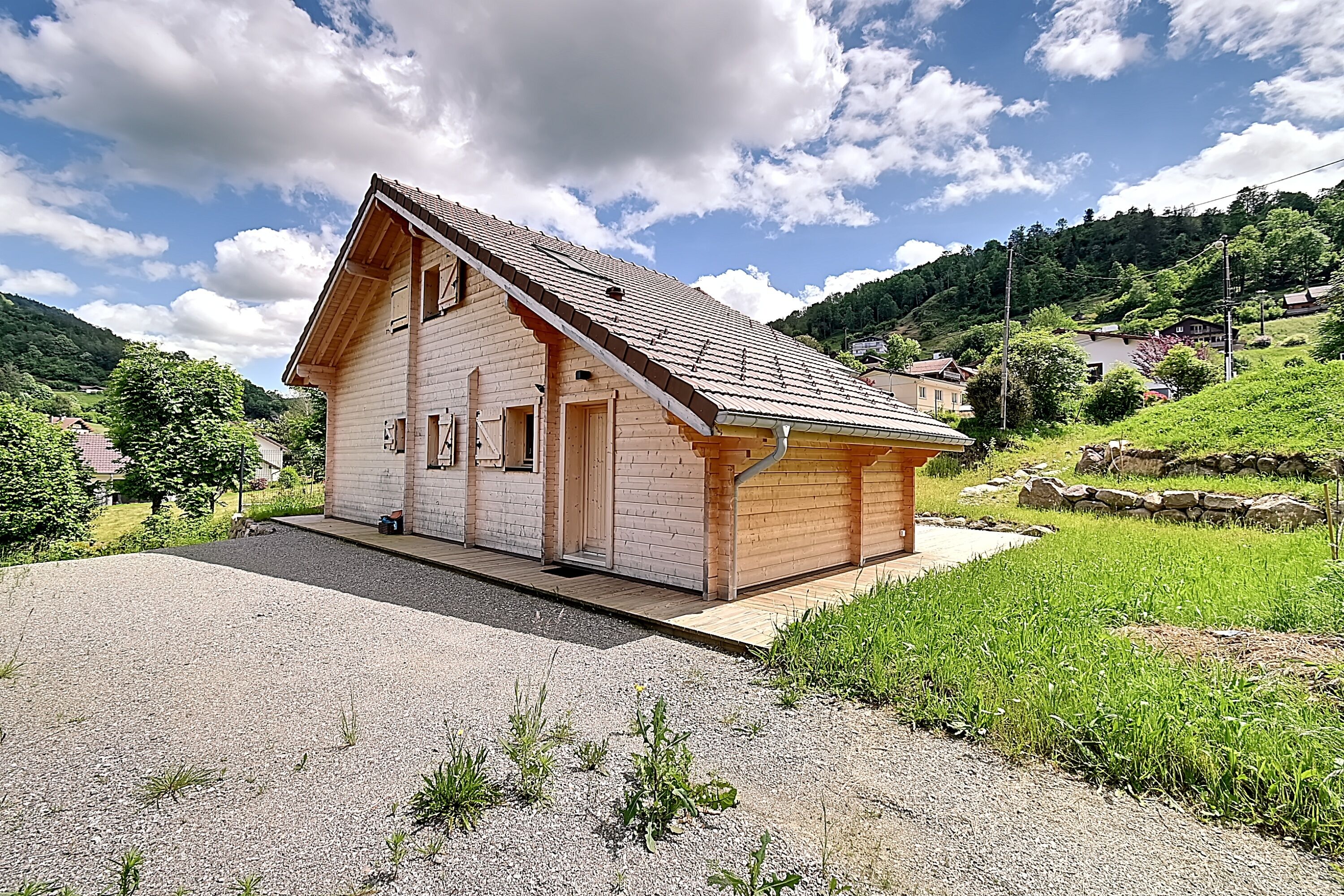Une maison en bois d’un seul étage, avec un toit en pente, un porche à l’avant et une allée gravillonnée.