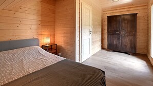 A wooden-paneled room with a bed, a wardrobe, and a small table with a lamp.