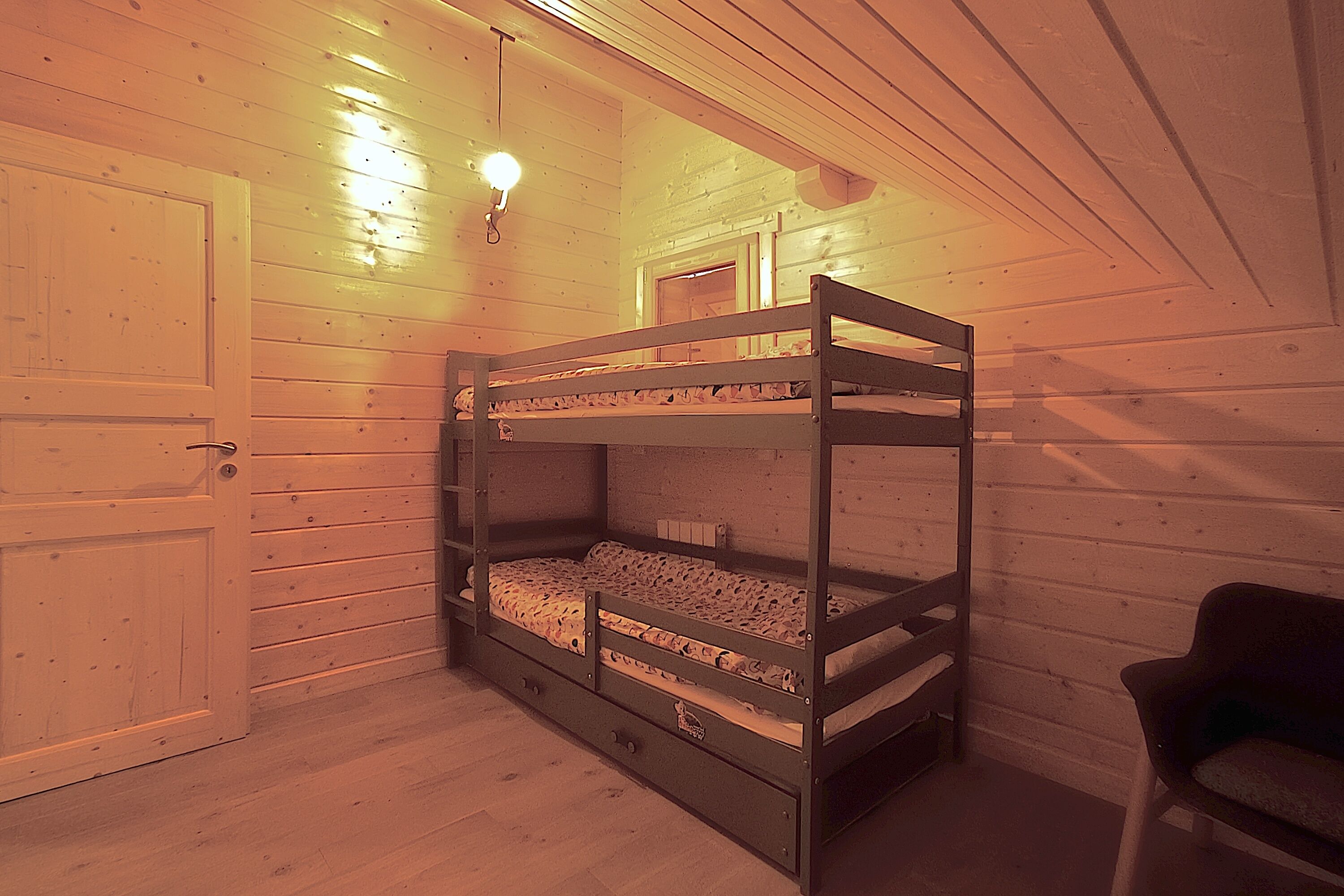A bunk bed in a room with wooden walls and a door.