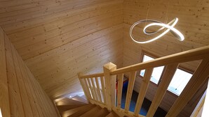 A wooden interior with a spiral staircase, wooden walls, and a hanging light fixture.