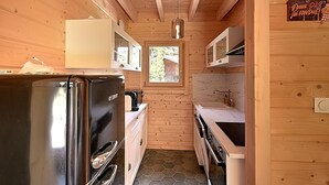 A compact kitchen with wooden walls, a stainless steel refrigerator, a microwave, and a sink.