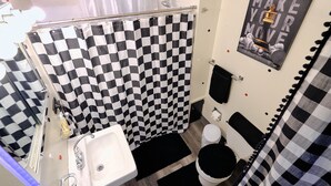 A bathroom with a checkered shower curtain, a white sink, a toilet, and a poster on the wall. - Trendy Downtown Nashua Getaway: Checkers-Themed 1 Bed/1 Bath! (Nashua)