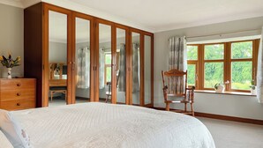 Un dormitorio con una cama grande, un armario, una silla y una ventana con vistas a zonas verdes.