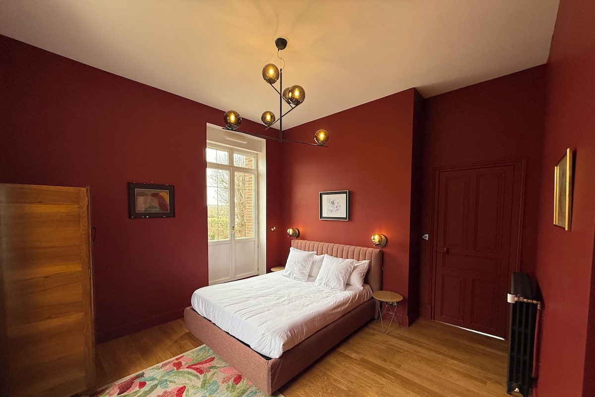 A bedroom with a bed, a wooden wardrobe, a door, and a window.