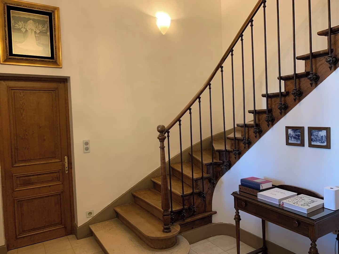 Una escalera de madera con barandilla, una puerta y un aplique en la pared.