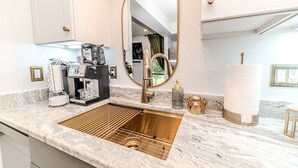 A modern bathroom with a marble countertop, a gold sink, a large mirror, and a coffee machine.