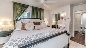 A bedroom with a large bed, green curtains, a ceiling fan, and a walk-in closet.