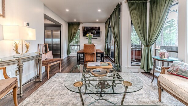 A modern living room with a glass coffee table, wooden furniture, and green curtains.