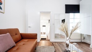 A modern living room with a brown leather sofa, a small rug, a vase with dried plants, a remote control, and a brass bowl on a wooden coffee table. - Beautiful Flat Near the Center 11 min  (London)