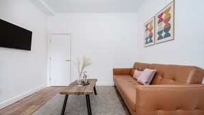 A modern living room with a brown leather sofa, a wooden coffee table, and two abstract paintings on the wall. - Beautiful Flat Near the Center 11 min  (London)